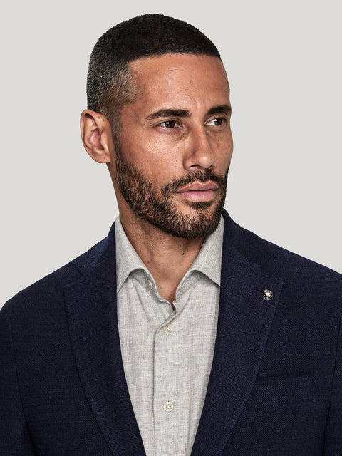 Man wearing navy blazer with notch lapels over light gray button-up shirt.