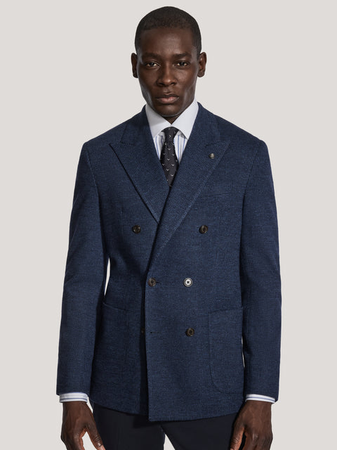 Navy blue double-breasted blazer with micro houndstooth texture, styled with light blue dress shirt and dark patterned tie.