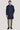 Man wearing dark blue wool coat with stand collar and button front over beige trousers and brown shoes.