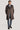 Taupe double-breasted trench coat with notch lapels and shoulder epaulettes worn over a light blue shirt and dark tie.