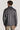 Man wearing grey herringbone shirt jacket with collar and button cuffs, shown from back.