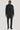 Navy twill topcoat with notch lapels, two-button closure, and removable bib insert worn over gray turtleneck and navy trouser