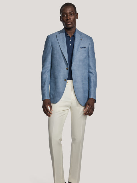 Man wearing light blue blazer with notch lapels and brown buttons over navy shirt, cream trousers, and black loafers.
