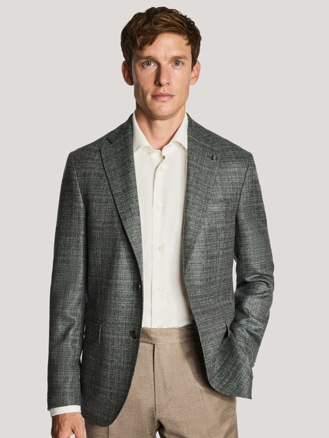 Green melange blazer with notch lapels and button closure worn over cream shirt and tan trousers.