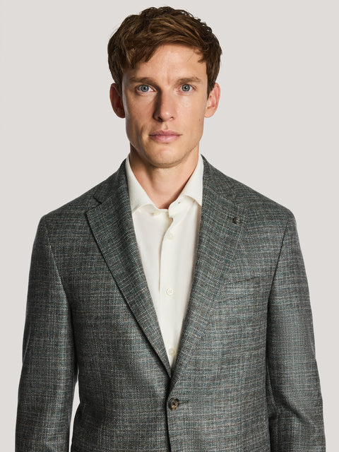 Green melange blazer with notch lapels worn over cream button-up shirt.