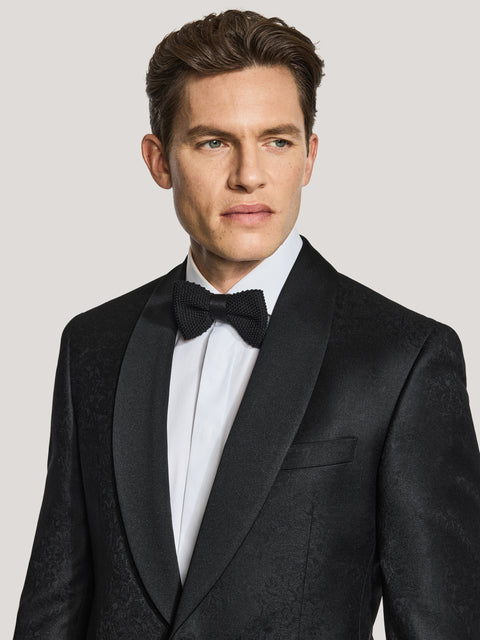 Black paisley dinner jacket with notch lapels, worn with white dress shirt and black bow tie.