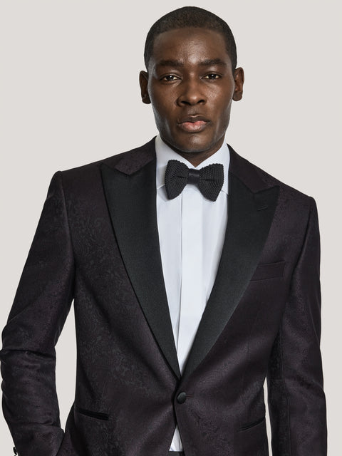 Man wearing burgundy paisley dinner jacket with notch lapels, white dress shirt, and black bow tie.